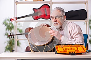 Old male repairman repairing musical instruments at workplace