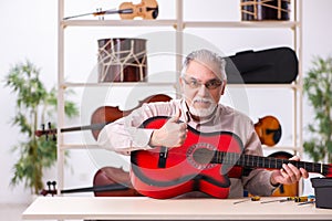 Old male repairman repairing musical instruments at workplace