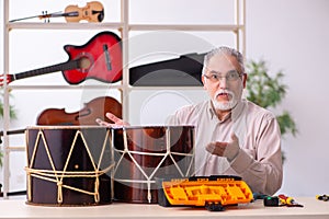 Old male repairman repairing musical instruments at workplace