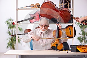 Old male repairman repairing musical instruments at workplace