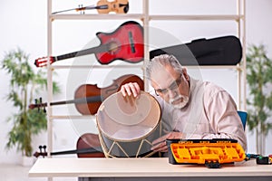 Old male repairman repairing musical instruments at workplace