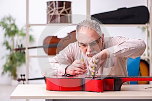 Old male repairman repairing musical instruments at workplace