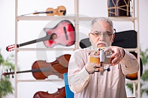 Old male repairman repairing musical instruments at workplace