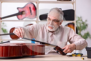 Old male repairman repairing musical instruments at workplace