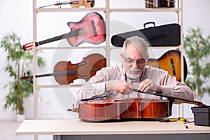 Old male repairman repairing musical instruments at workplace