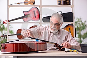 Old male repairman repairing musical instruments at workplace