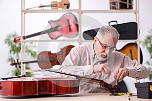 Old male repairman repairing musical instruments at workplace