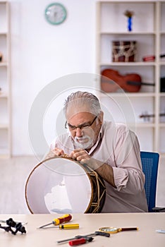 Old male repairman repairing musical instruments at workshop