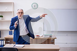 Old male teacher holding penlight in the classroom
