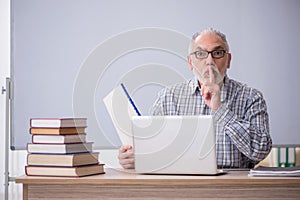Old male teacher sitting in front of whiteboard