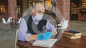 Old male teacher works with protective mask and gloves in university canteen or college cafeteria