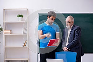 Old male teacher and young male student in front of blackboard