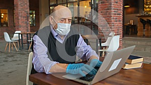 Old male teatcher with protective mask and gloves works in university canteen or college cafeteria