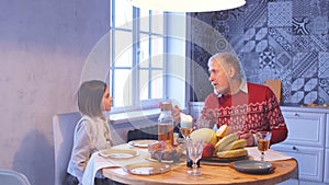 Old man with adorable girl is sitting at the table and chatting