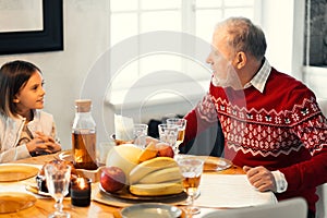 Old man with adorable girl is sitting at the table and chatting