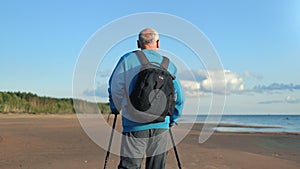 Old man backpacker cardio training with Scandinavian walking stick contemplate sunny sea beach