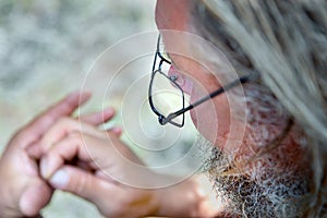 An old man with a beard and glasses looks at his hands