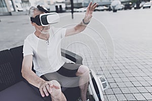 An old man with a beard sits on a sofa in the street. On it the helmet of virtual reality