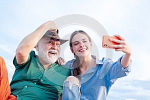 Old man and beautiful young girl are hugging and making selfie. Granddaughter with elderly kind grandfather. Relatives