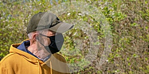 Old man in black disposable face mask looks at garden trees