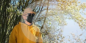 Old man in black disposable mask stands near garden tree