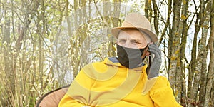 Old man in black gloves and mask sits in garden closeup