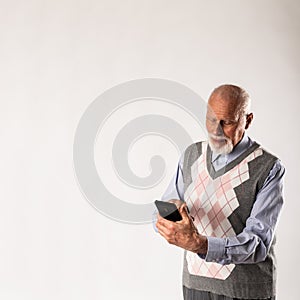 Old man in blue is using a smart phone on gray background with copy space
