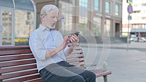 Old Man Browsing Internet on Smartphone while Sitting Outdoor on Bench