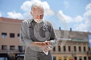 Old man cleaning hands with wet wipes on street