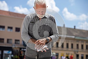 Old man cleaning hands with wet wipes on street