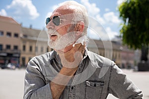 Old man cleaning neck and sweat with wet wipes outdoor on hot summer day