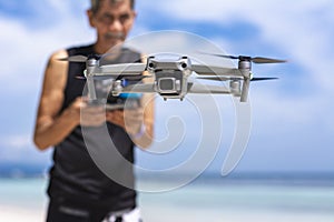 An old man controlling a small drone at the beach. A Hobbyist drone operator flying outdoors