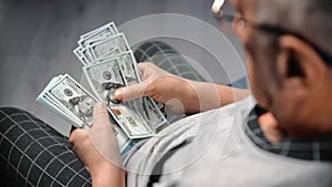 Old man counting dollars, holding banknotes in hands, view from shoulder, rich retiree man in home