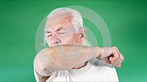 Old man covers his mouth with his arm and coughs