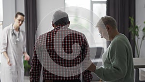 Old man with crutches helped by his wife and doctor