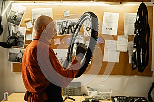 Old man Cycling mechanic checking bicycle wheel in authentic workshop. Garage interior with tools. Focused caucasian