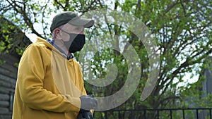 Old man in disposable mask stands near fence talking