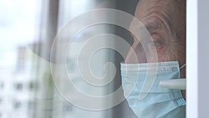 Old man in disposable mask waves hand at plastic window