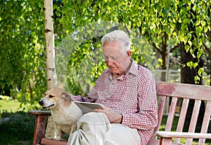 Old man with dog and tablet in garden