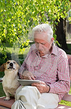 Old man with dog and tablet in garden