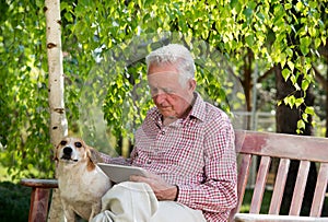 Old man with dog and tablet in garden