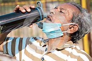 Old man drinking water from bottle by placing mask below face during hot sunny day - Concept of healthcare, medical, thirsty on