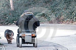 Old man drives an electric wheelchair and is accompanied by his faithful dog