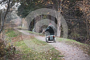 Old man drives with an electric wheelchair along a path in autumn