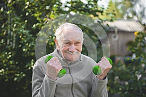 Old man with dumbbells. The fitness of the person engaged in in the garden. Active old age, healthy lifestyle