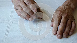 The old man is eating a piece of rye bread. Close-up shot of an elderly man taking a piece of bread from the table. The theme of n