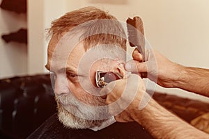 Old man enjoing haircut by a master in a barbershop.  An old man gets a stylish haircut