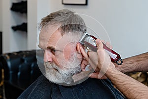 old man enjoing haircut by a master in a barbershop. An old man gets a stylish haircut