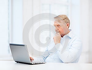 Old man in eyeglasses working with laptop at home