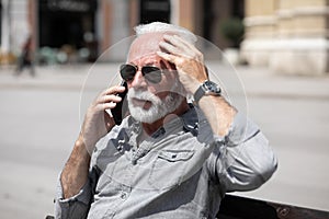 Old man forget and remember something, speak on smartphone, seating on bench,  stock photo